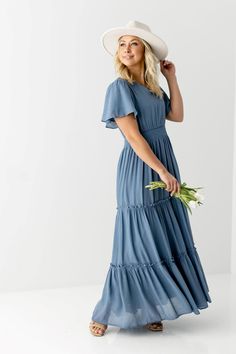 The Valorie Maxi Dress was made for warm days in the sun! This long, tiered dress is cut from lightweight fabric and is fully lined to let you move through the day in breathable all-day comfort. The pullover style features a smocked waist, flutter sleeves and a v-neckline. The perfect modest dress for Easter Sunday, a photoshoot, or summer soiree! Pair it with slide sandals or wedge heels and complete your look with a woven bag and stylish shades when out and about! 100% Polyester Wash Inside Ou Long Tiered Dress, Evening Dresses Wedding, Casual Bridesmaid Dresses, Dusty Blue Dress, Modest Maxi Dress, Long Evening Dresses, Modest Summer Outfits, Long Blue Dress