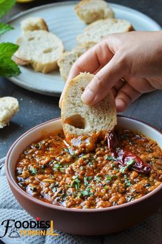 a person dipping some bread into a bowl of soup with other food on the side