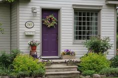 a purple front door and steps leading to a white house with flowers on the porch