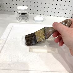 a person holding a paint brush over a white surface