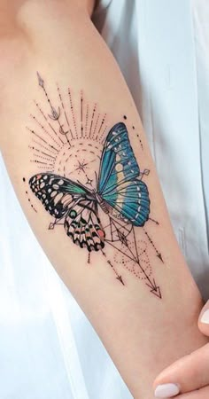 a blue butterfly tattoo on the arm with an arrow and sunburst behind it