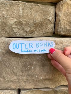 a person holding up a sticker that says outer banks on each side of a stone wall