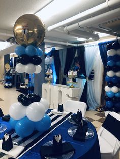 balloons are hanging from the ceiling in an event room with blue and white tables cloths