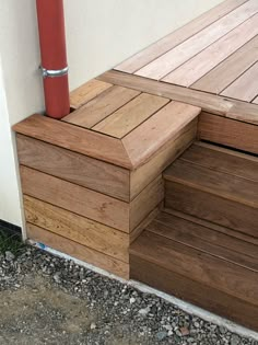 a wooden step next to a white wall and red post on the side of a building