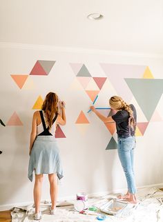 two women are painting triangles on the wall