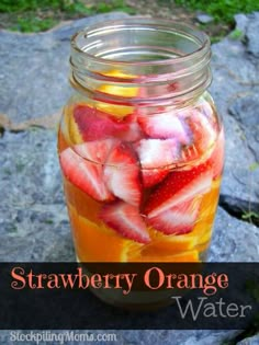 a mason jar filled with sliced strawberries and oranges on top of a rock