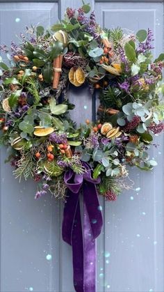 a wreath is hanging on the door with purple ribbon and leaves around it, as well as other decorations