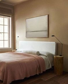 a bed sitting in a bedroom under a window next to a wooden table and lamp