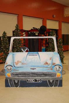 an old blue car is in the middle of a room with christmas trees and decorations