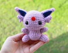 a hand holding a small crocheted toy in the shape of a cat with red nose and tail