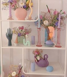 a shelf filled with vases and flowers on top of white shelving units in a room