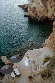 a bride and groom standing on the edge of a cliff by the ocean with umbrellas