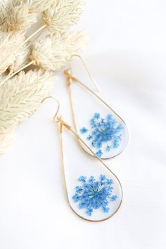 the earrings are decorated with blue flowers and gold wire, along with some dried plants