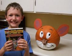 a young boy holding up a book next to a pumpkin shaped like a mouse head