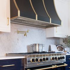 a stove top oven sitting inside of a kitchen next to white cabinets and drawers with gold trim