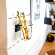 three pencils are in a mason jar hanging on the wall