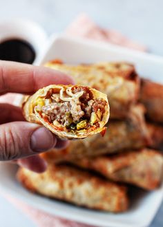 a hand holding up a burrito in front of some other food items on a plate