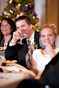 a bride and groom sitting at a table with wine glasses in front of their faces