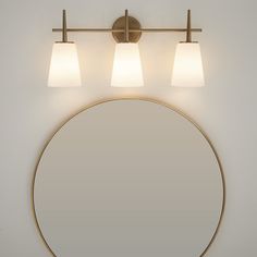 a bathroom mirror with three lights and a round light fixture on the wall above it