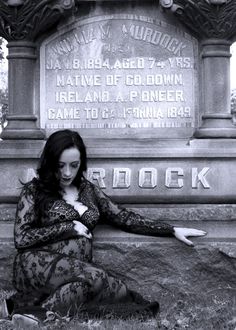 a woman sitting on the ground in front of a grave with her arms folded out