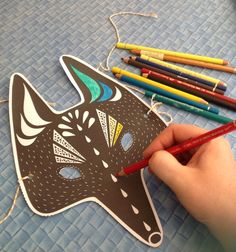 a person is holding a pencil and drawing a mask with colored crayons on the table