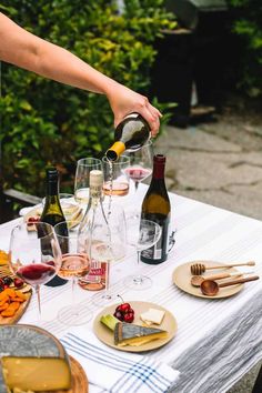 a person pours wine into glasses on a table with food and utensils