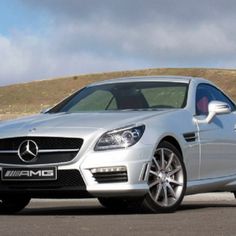 a silver mercedes slk parked on the side of a road with hills in the background