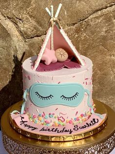 a pink birthday cake with a sleeping eye on top and a teepee tent in the background