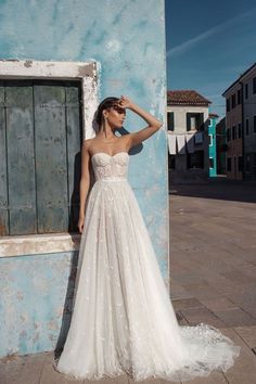 a woman standing in front of a blue wall wearing a wedding dress and holding her hand on her head