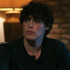 a man with curly hair sitting in front of a lamp