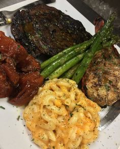 a white plate topped with macaroni and cheese next to meat, asparagus and broccoli