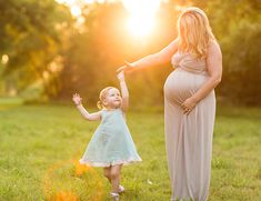 a pregnant woman holding the hand of her child's hand while standing in a field