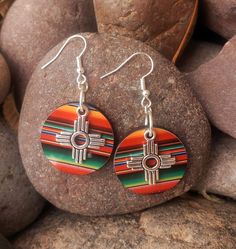 Zia Round Serape Earrings, New Mexico Serape Earrings, Southwestern Earrings, Western Earrings, Zia Jewelry, New Mexico Jewelry.  These lightweight earrings are perfect statement of the Southwest.  Earring is a lightweight wood printed with a vibrant serape print.  Final touch to adorn these precious earrings is a stainless-steel Zia charm.  These will for sure be your favorite earrings.  Perfect with any outfit and so light you won't even remember you are wearing them.  Get your today, they com New Mexico Jewelry, Southwestern Teardrop Jewelry For Festivals, Multicolor Southwestern Teardrop Jewelry, Multicolor Southwestern Style Teardrop Jewelry, Southwestern Style Multicolor Teardrop Jewelry, Festival Concho Dangle Jewelry, Southwestern Multicolor Teardrop Earrings, Southwestern Style Concho Drop Earrings, Traditional Concho Earrings For Gift