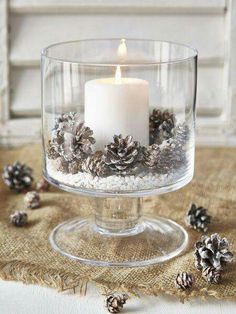 a glass bowl filled with pine cones and a lit candle on top of a table