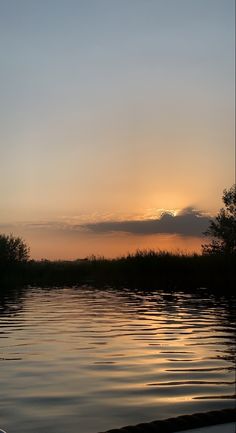 the sun is setting over water with trees in the background