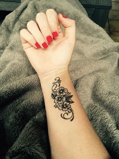 a woman's arm with a flower tattoo on her left wrist and red nail polish