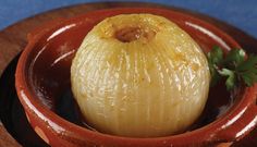 an onion is in a bowl on a wooden plate with a garnish sprig