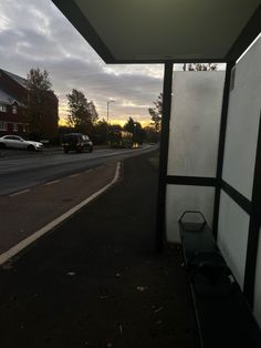 an empty bus stop sitting on the side of a road with cars parked in front of it