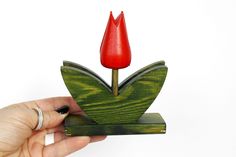 a hand holding a small piece of wood with a red flower on the top and bottom