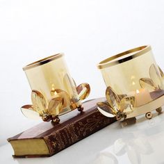 two golden glass candle holders sitting on top of a book