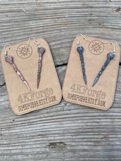 two earrings with different designs on them sitting next to each other in front of a wooden table