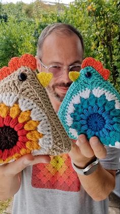 a man holding two crocheted bird ornaments in front of his face and smiling at the camera