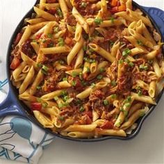 a skillet filled with pasta, meat and veggies on top of a table