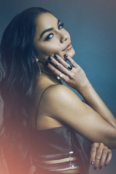 a woman posing with her hand on her face and wearing black nail polish, in front of a blue background