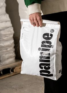 a person holding a white bag with the word shopping printed on it, while standing in front of stacks of bags