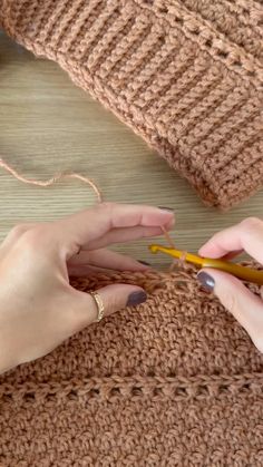 two hands crocheting the ends of a knitted sweater