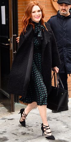 a woman in a black coat and green dress is walking down the street with her handbag