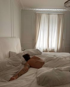 a naked woman laying on top of a bed in a room with white walls and curtains