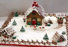 a gingerbread christmas village is displayed on a white tablecloth with red and green trimmings