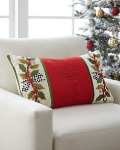 a white chair with a red pillow on it in front of a christmas tree and window